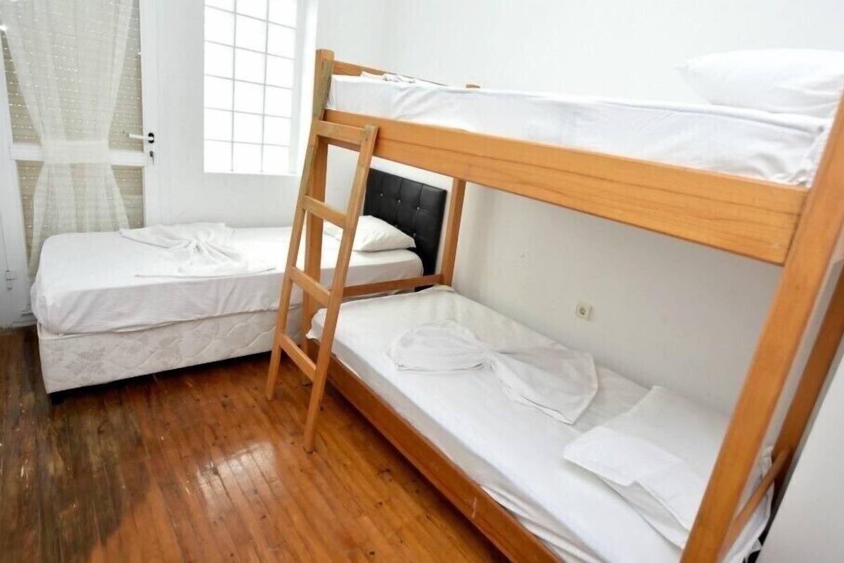 A dormitory room with two bunk beds, a wooden ladder, and a window with a grid pattern.