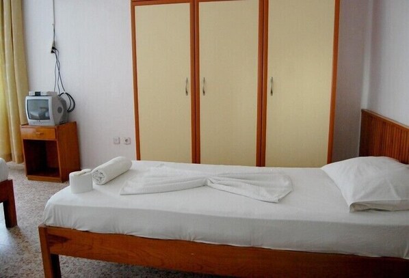 A single bed with white linens, a wooden headboard, and a wooden nightstand with a television. - Cavdar Hotel (Ayvalik)