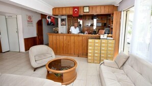 Un área de recepción con mostrador de madera, un reloj y una bandera. Hay dos sofás y una mesita de centro.