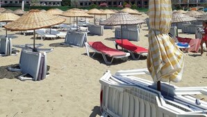 Una playa con tumbonas y sombrillas, un edificio al fondo y una colina.