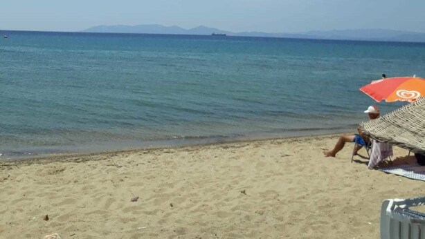 Una playa con cielo despejado, mar tranquilo y una cadena montañosa a lo lejos.