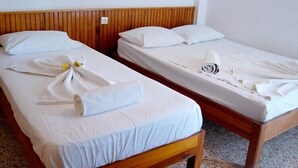 Dos camas individuales con cabeceros de madera y ropa de cama blanca, una con una toalla y un arreglo floral.