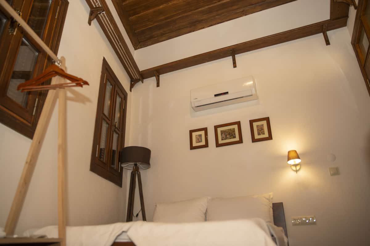 Ein Schlafzimmer mit einem Bett, einer Pendelleuchte, einer Wand-Klimaanlage und einem Fenster mit Holzrahmen.