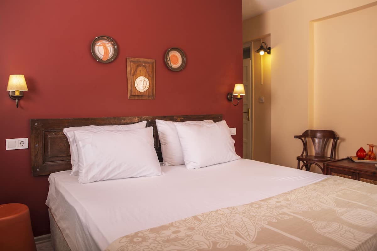 Ein ordentlich bezogenes Bett mit weißen Laken in einem Raum mit roten Wänden und zwei Wandleuchten.