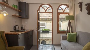 Un espace de vie compact comprenant un coin cuisine, un canapé, une table à manger et une vue sur une zone extérieure accessible par une porte, avec un balcon.