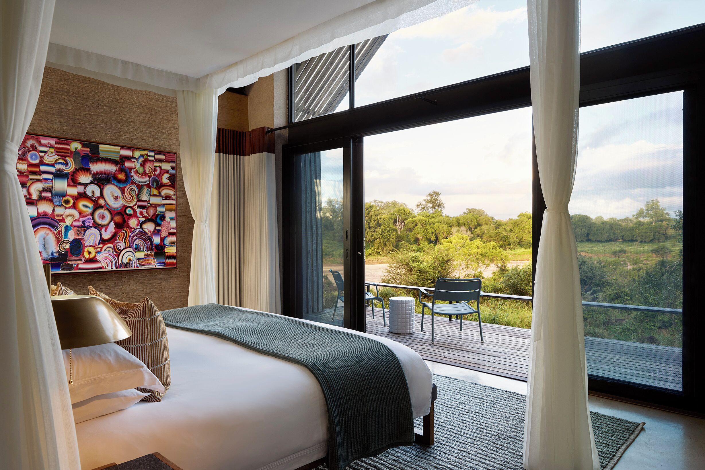 Quarto com uma cama grande, vista para o exterior e varanda com cadeiras.