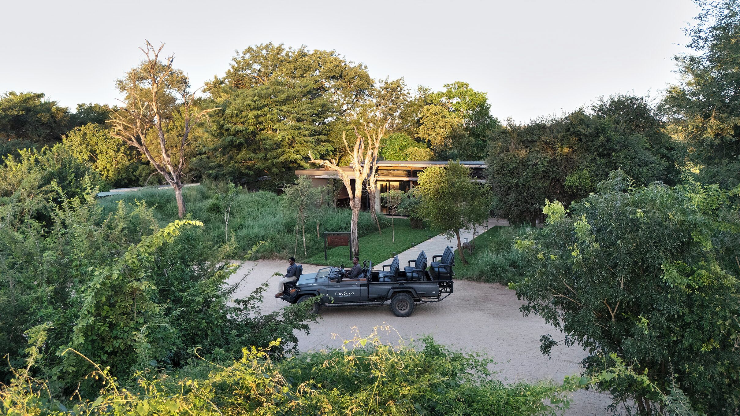 A safari vehicle parked in a natural setting with trees and a building in the background.