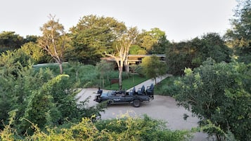 A safari vehicle parked in a natural setting with trees and a building in the background.