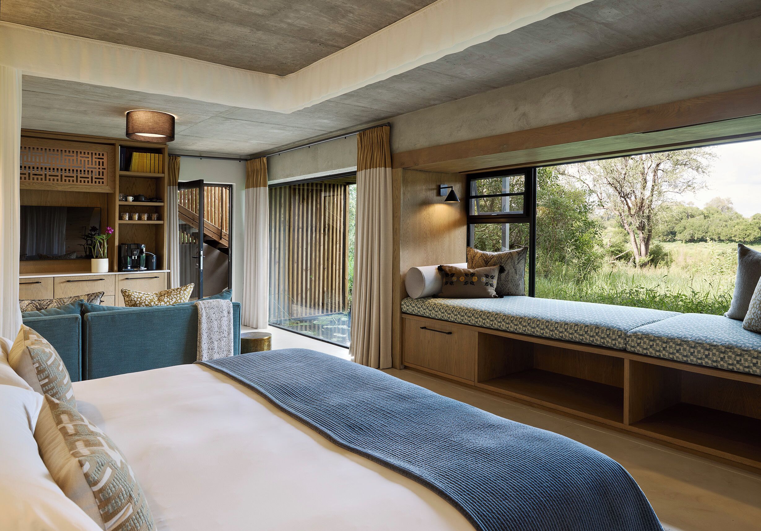 Une chambre dotée d’un grand lit, d’un coin salon avec des coussins, d’un bureau intégré et offrant une vue sur l’extérieur.