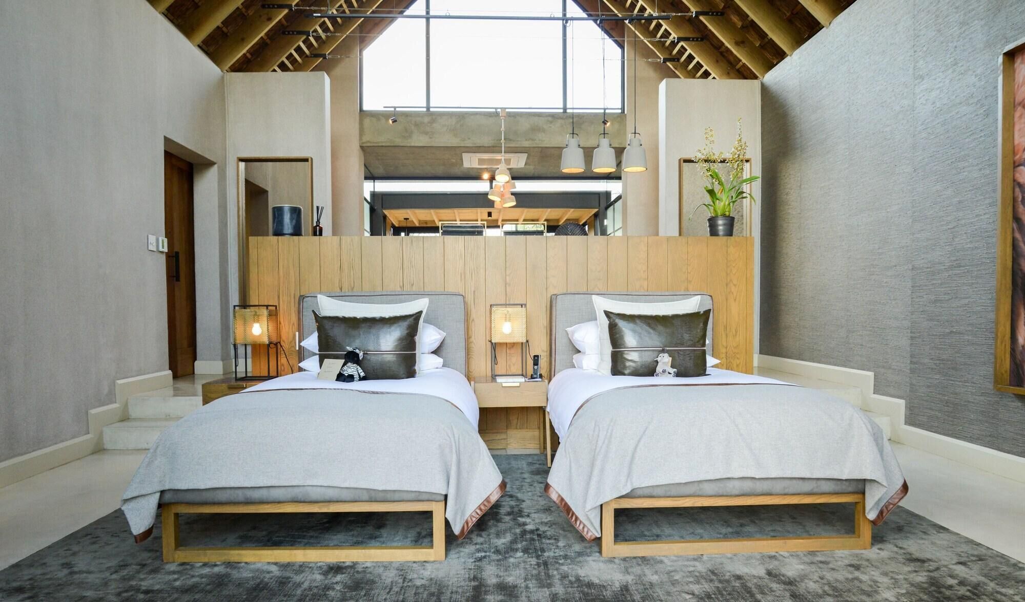 A modern bedroom with two beds, a skylight, and a wooden ceiling.