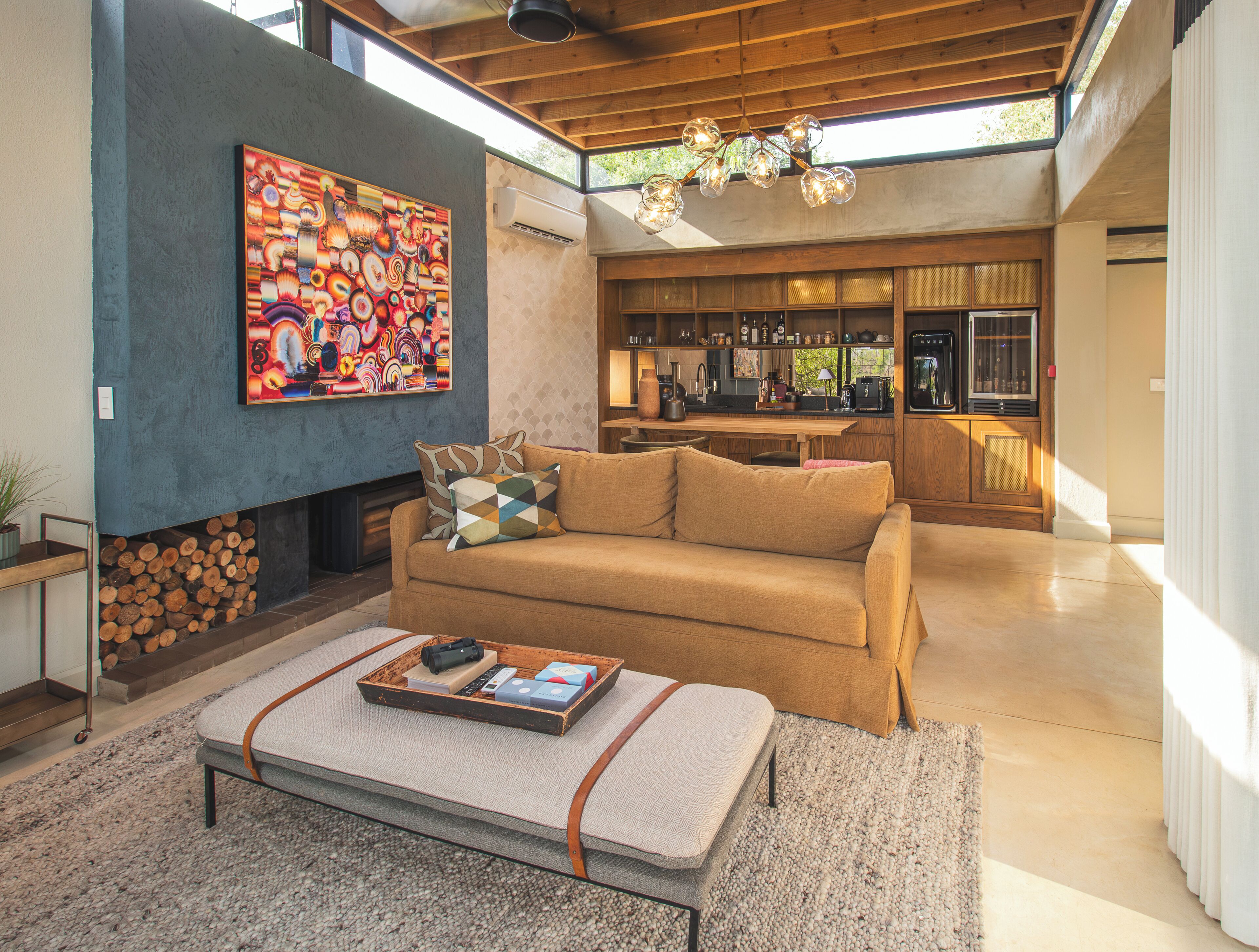 A spacious living area with a modern kitchen in the background, a large painting on the wall, and a cozy seating arrangement.