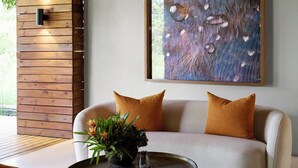 A modern living room with a sofa, a coffee table with a plant, a hanging light fixture, and a large abstract painting on the wall.