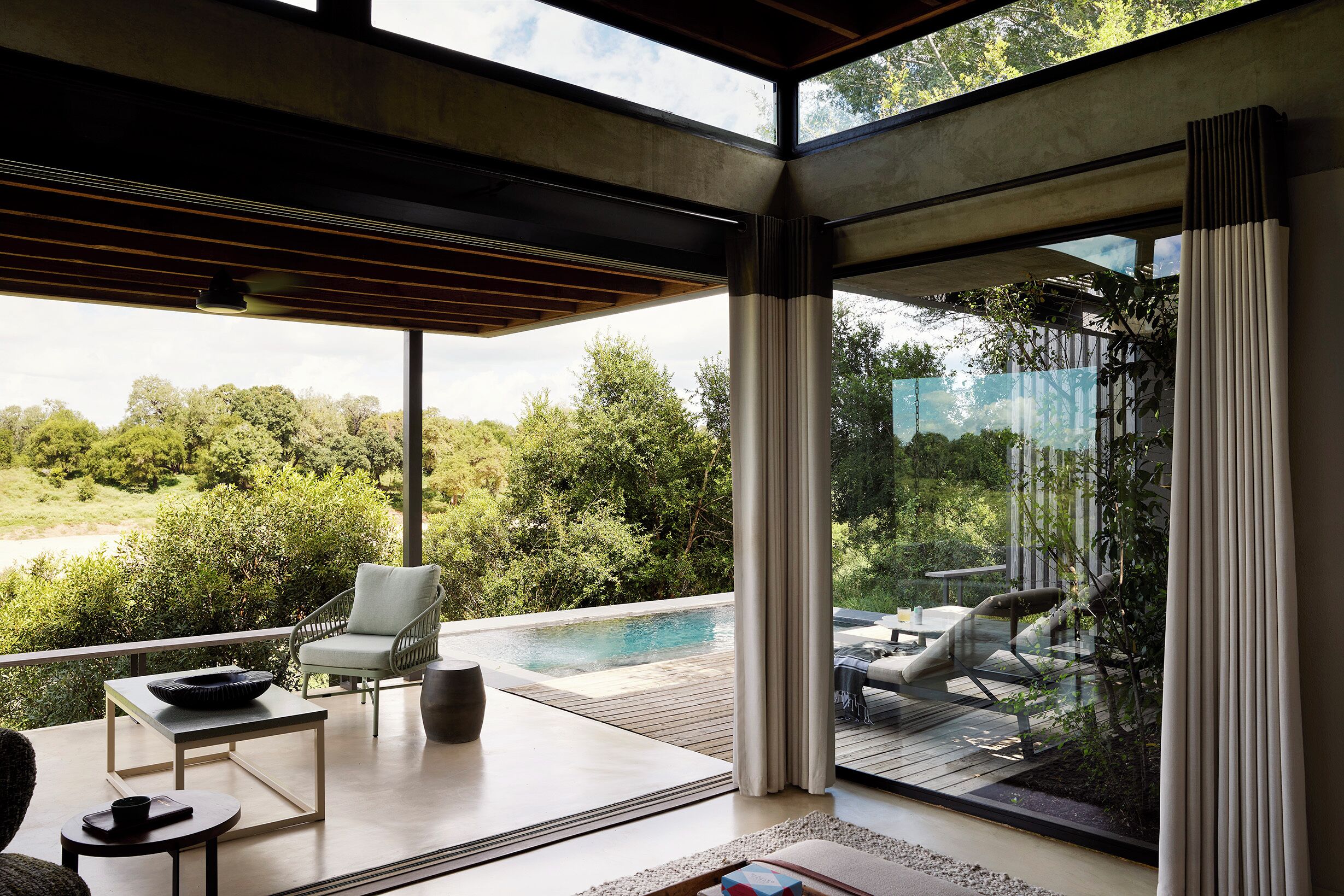 A modern outdoor lounge area with a pool, seating, and a view of the surrounding greenery.