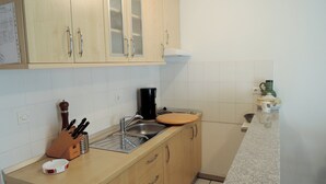 A kitchen with wooden cabinets, a sink, a coffee maker, and a countertop with a knife block and a mug. - Apartments Mermaid (Malinska-Dubasnica)