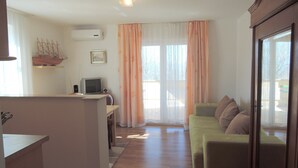 A compact living space with a kitchenette, a television, a sofa, and a window with curtains. - Apartments Mermaid (Malinska-Dubasnica)