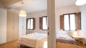 Un dormitorio con cama, mesita de noche, lámpara, armario y ventana con contraventanas.