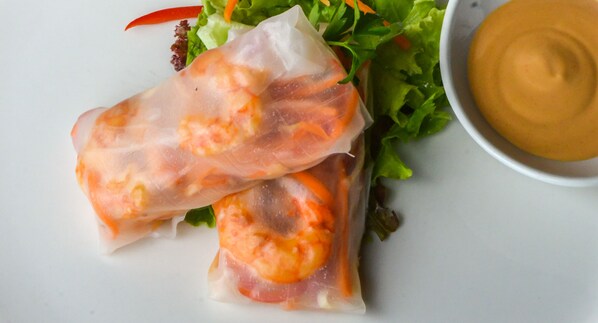 Dos rollitos de primavera de camarón y lechuga, acompañados de salsa para mojar.
