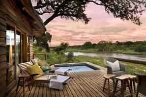 Eine Holzterrasse mit Liegestühlen, einem Whirlpool und Blick auf einen Fluss und Bäume.