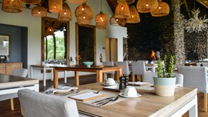 Ein Restaurant mit Holztischen, hängenden Korbstühlen und einer Steinsäule im Hintergrund.