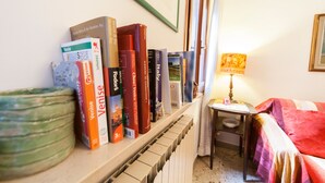 Ein Bücherregal mit Reisebüchern, eine Lampe und ein Bett mit einer farbenfrohen Decke.