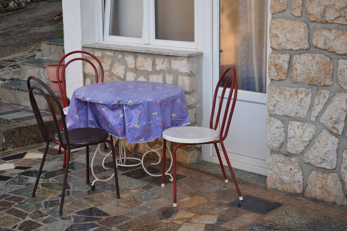 A table with a purple tablecloth, two chairs, and a stone wall.