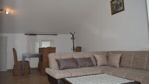Olohuoneessa on sohva, pöytä ja tuoli. Seinällä on taulu ja huoneessa on lamppu.