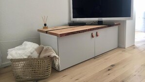 A minimalist living room with a flat-screen TV on a wooden cabinet, a wicker basket, and a white sofa.