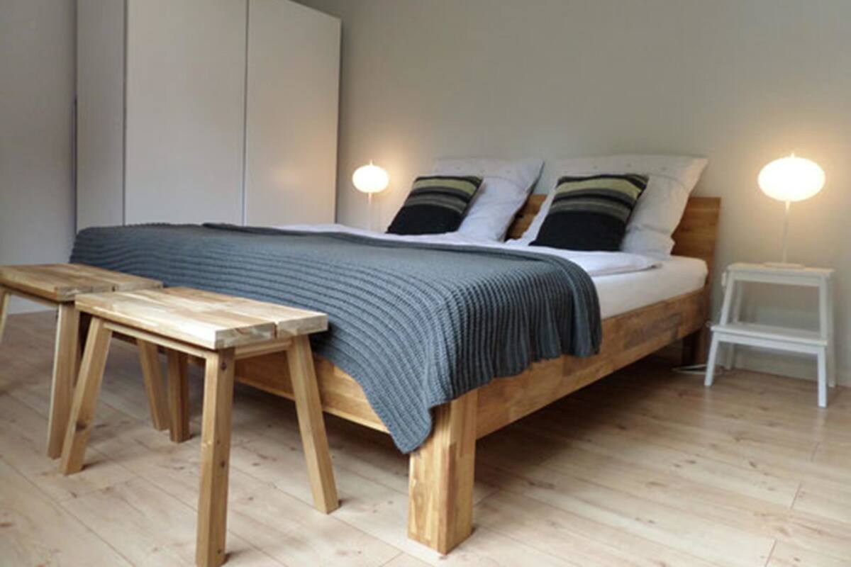 A bedroom with a wooden bed, a bedside table, a nightstand, and a wardrobe.