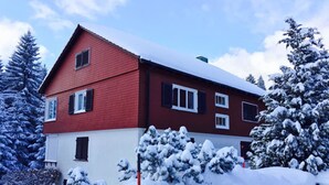 A two-story house with a red and white exterior, surrounded by snow-covered trees and a snowy landscape.