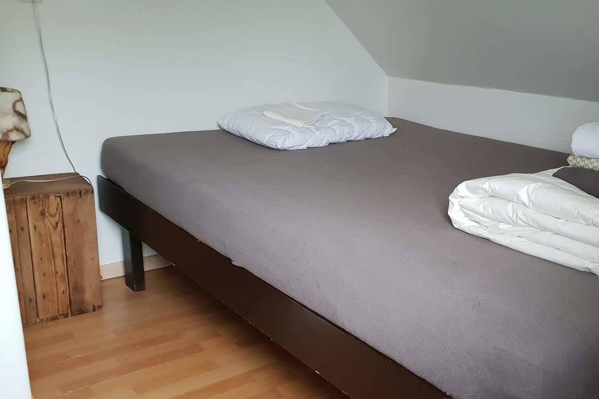 Een enkel bed met een grijze matras en witte beddengoed, inclusief een opgevouwen deken en kussens.