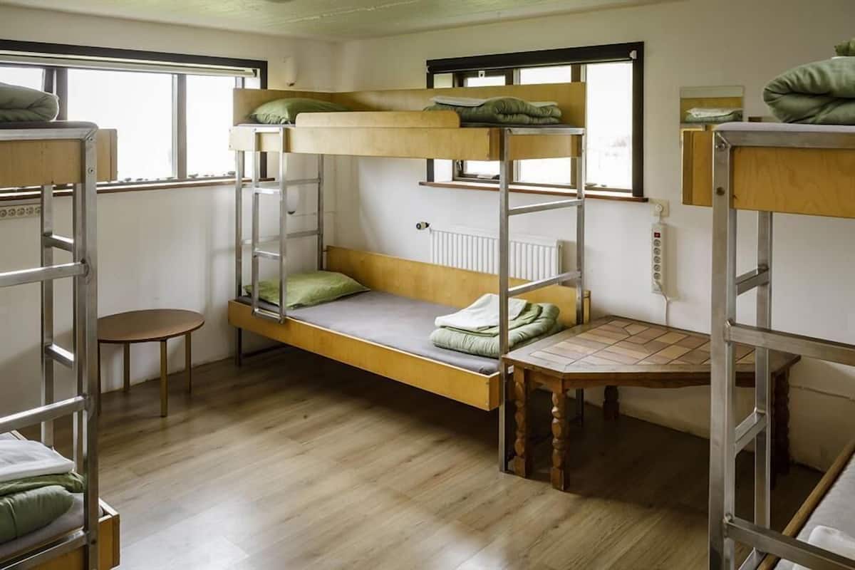 Een slaapkamer met een stapelbed, een houten vloer, een klein tafeltje en een raam.