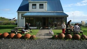 A building with a large glass front, outdoor seating, and a gravel area with large decorative pots. - Vik HI hostel (Vik I Myrdal)