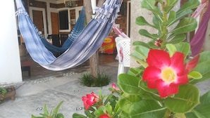A hammock hanging between two trees, a red flower in the foreground, and a building entrance with a tiled floor. - Pousada Brisa Da Serra em Sobral (Sobral)