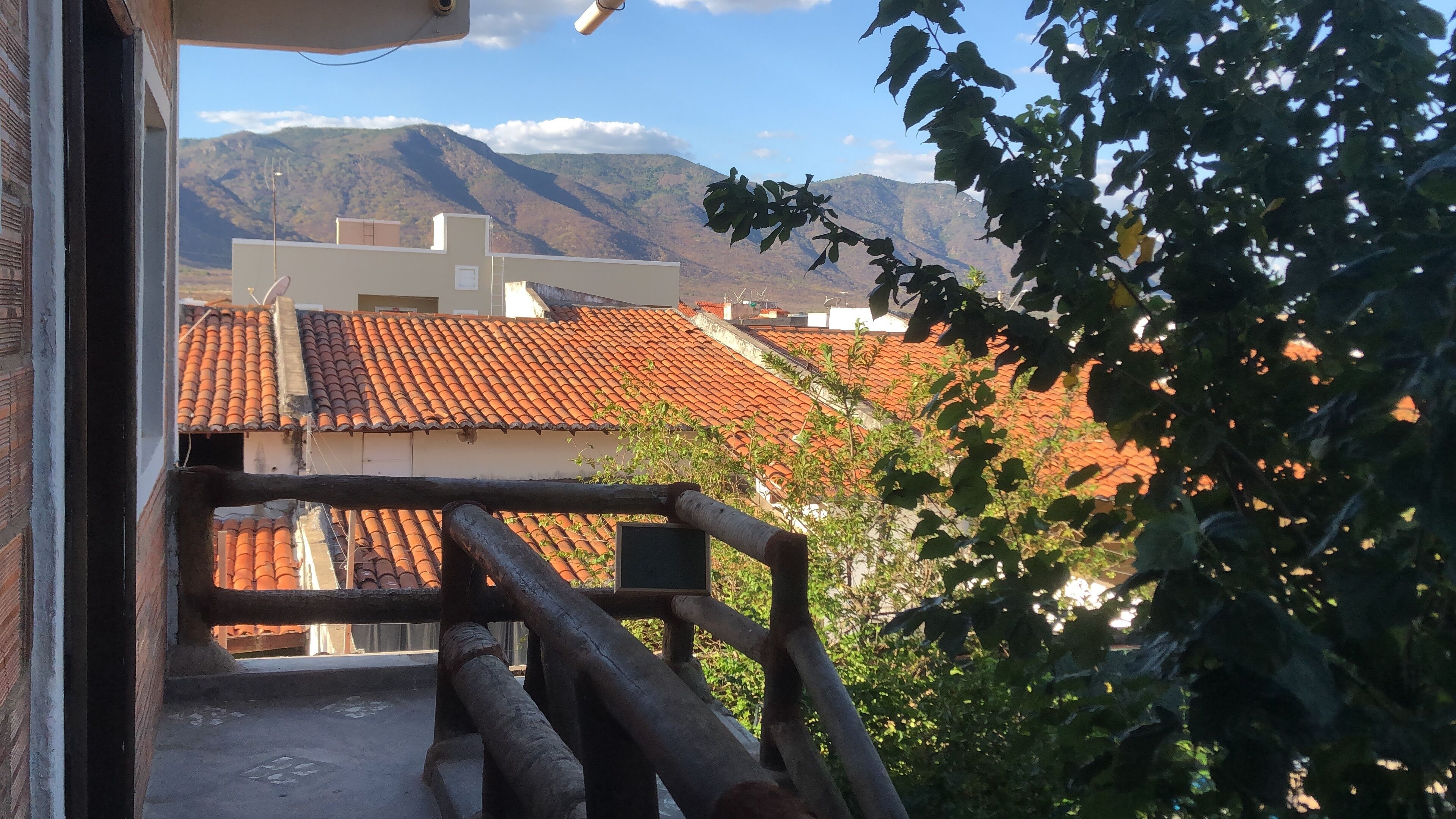 Uma varanda com vista para edifícios de telhado em terracota e montanhas ao fundo.