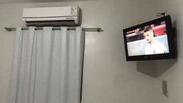 Una habitación con aire acondicionado blanco, cortina y televisor con un evento deportivo.