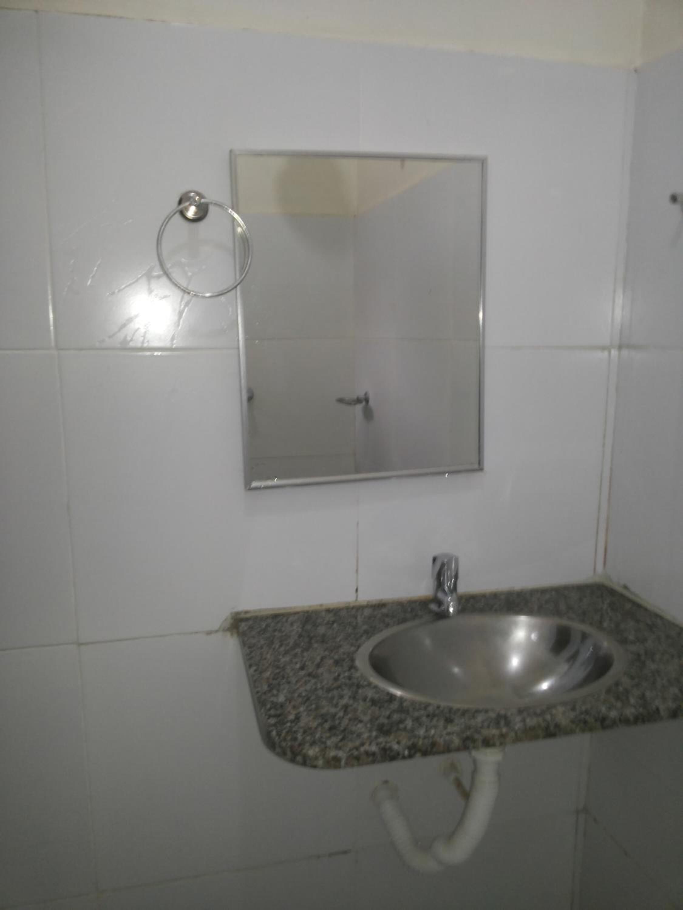Un baño con lavamanos, espejo y argolla para toallas.