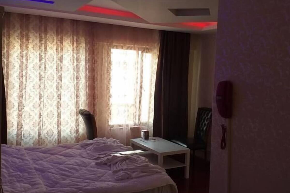 A hotel room with a bed, a desk, and a chair. There is a window with curtains and a phone on the wall.