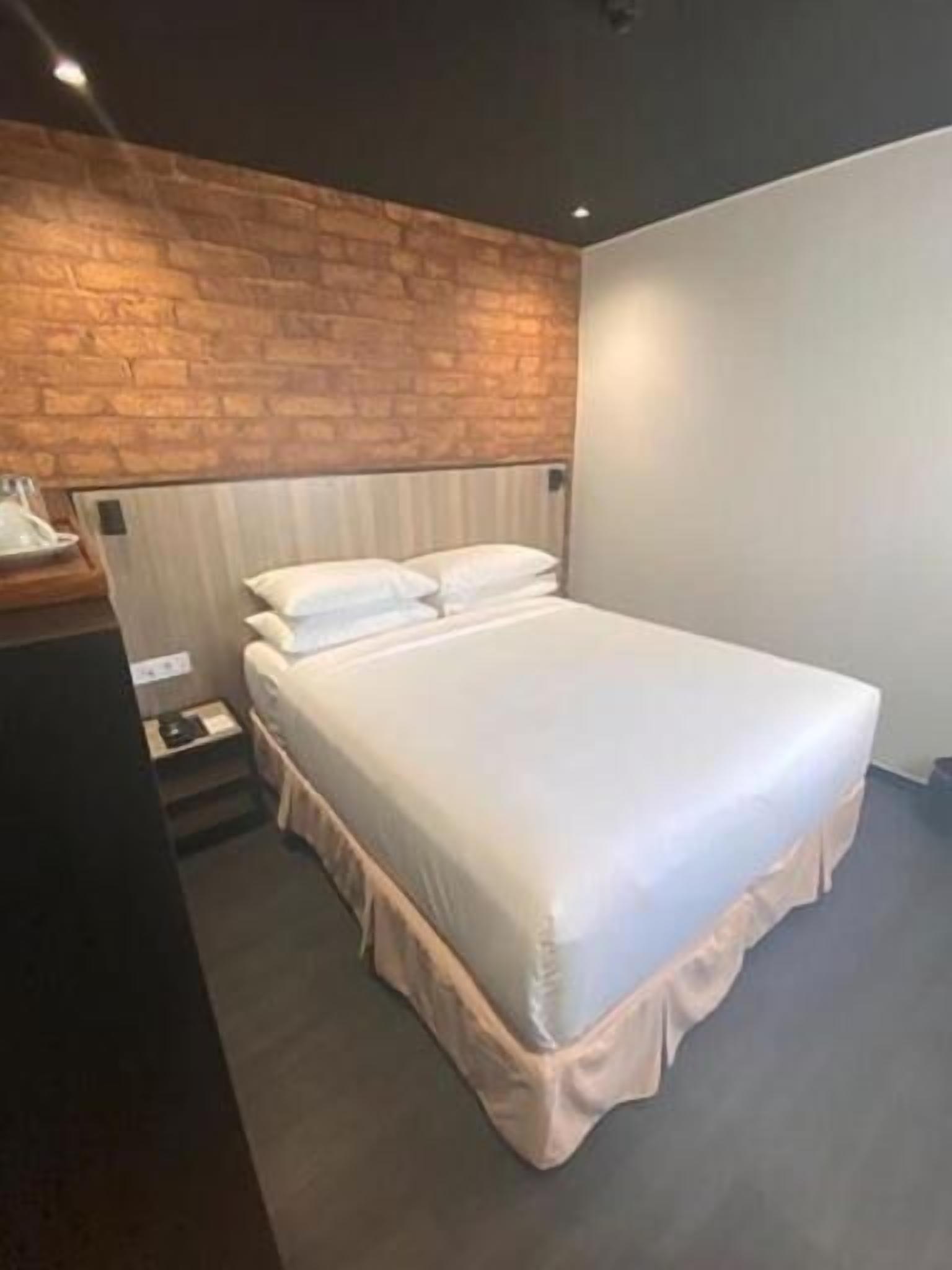 Ein modernes Schlafzimmer mit einer Ziegelwand als Blickfang, einem großen Bett mit Überhang und einem Nachttisch mit Lampe.