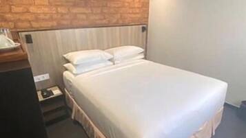 A modern bedroom with a brick accent wall, a large bed with a skirted base, and a bedside table with a lamp.