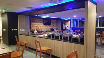 Zona de buffet amb taulell, cadires i cuina al fons.