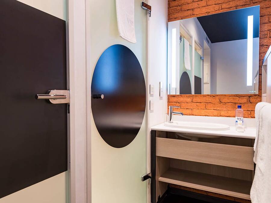 A modern bathroom with a black door, a round mirror, a sink, and a towel hanging on the wall.
