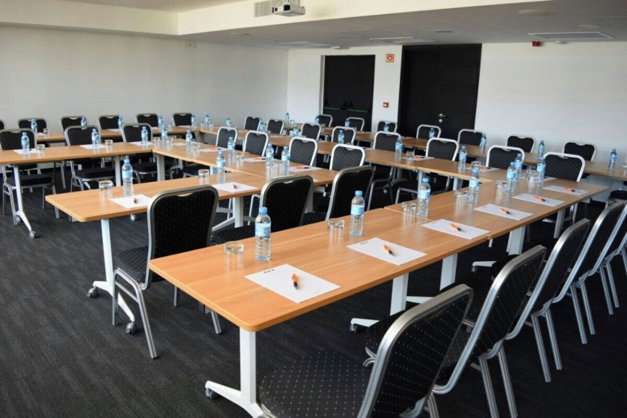 A conference room with multiple tables and chairs, equipped with water bottles and pens.