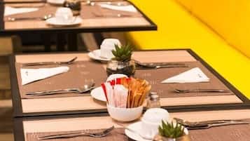 A dining area with tables set for service, each with a bowl of bread, a small plant, and a salt shaker.