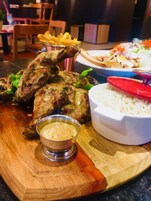 Una mesa de madera con carne a la parrilla, un tazón de arroz, un recipiente pequeño de salsa y una porción de papas fritas.