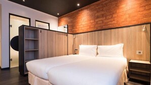 Una habitación de hotel moderna con una cama grande, paneles de madera en las paredes, un armario empotrado y una mesita de noche pequeña.