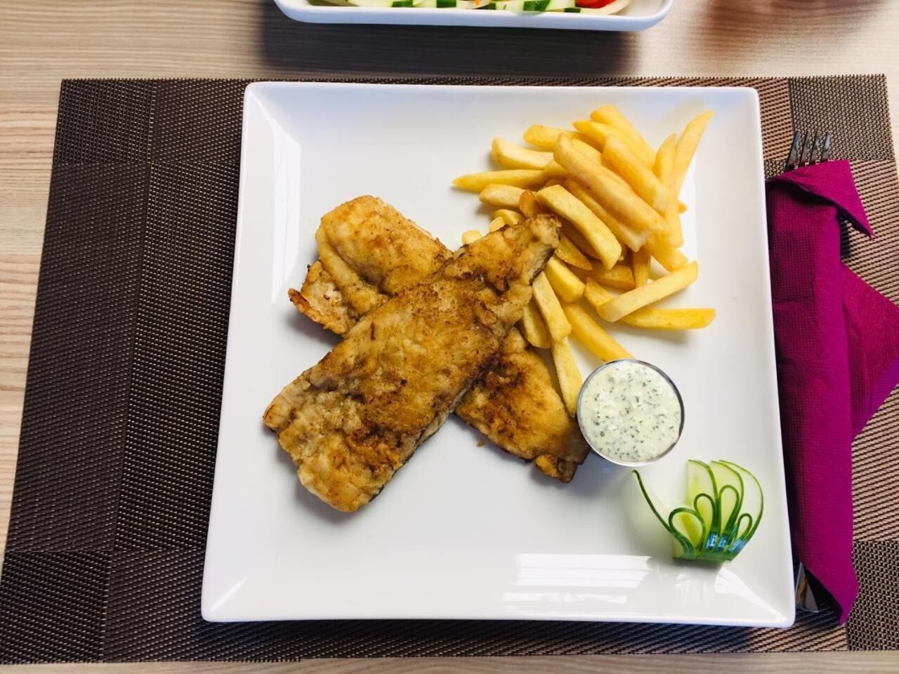 Un plato blanco con filetes de pescado rebozado, papas fritas y un recipiente pequeño con salsa.