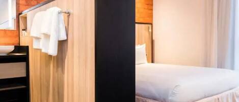 Habitación de hotel con una cama, pared de madera y baño con lavamanos y toallero.