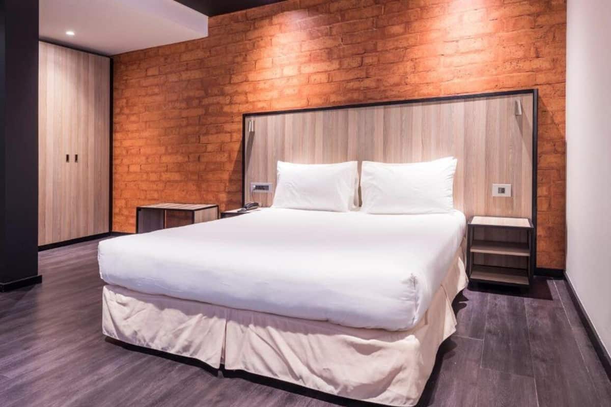 Quarto moderno com uma cama grande, painéis de parede de madeira e piso escuro.