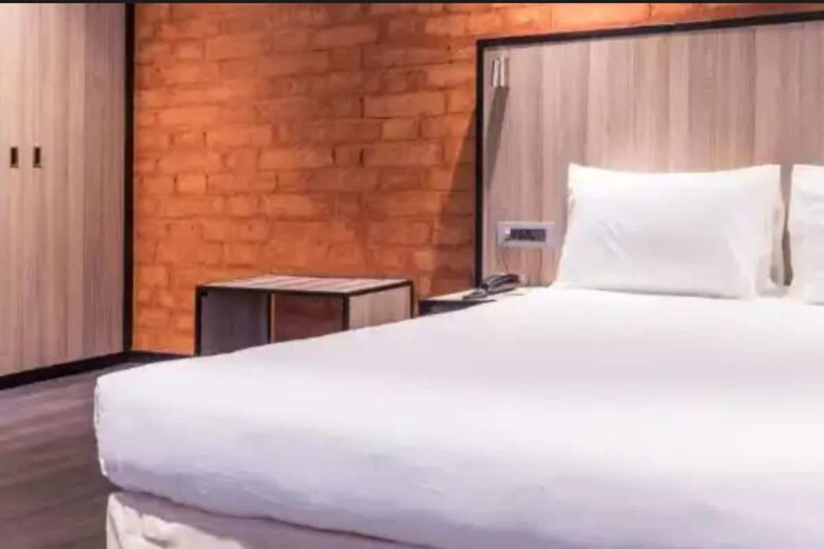 Quarto de hotel moderno com uma cama grande, cabeceira de madeira e parede decorada com tijolos.
