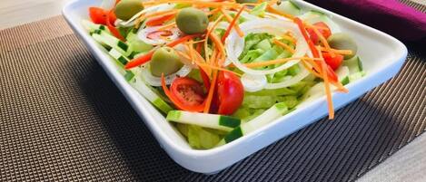 A rectangular white plate with a salad on a table.